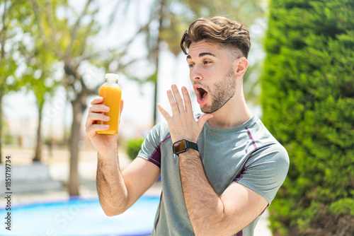 Photography Young handsome sport man holding an orange juice at outdoors with surprise and s