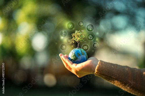 Close up of a hand holding a small globe with a growing tree surrounded by digital ESG icons for sustainability, environmental protection, and green energy concept