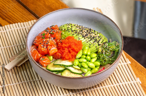 Poke bowl with salmon, avocado, edamame beans on wooden background.Trendy healthy sea food plate.