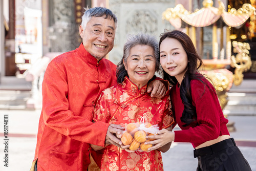 During the Lunar New Year at a beautiful Chinese temple, a cheerful teenage daughter presents her parents with oranges, symbolizing love and respect. Together, they cherish this festive tradition.