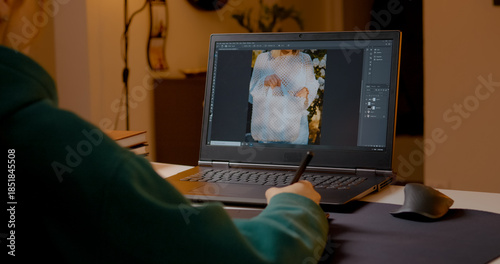 Woman is diligently editing images on her laptop using a graphics tablet in her home studio. Her focus on the screen illustrates the creative process of design work.