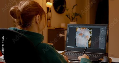 Woman is engaged in the creative process of editing images on her laptop using a graphics tablet. Her home studio is warm and inviting, showcasing her design skills.