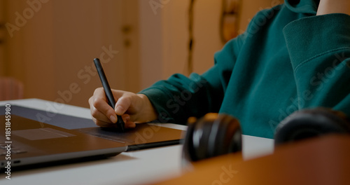 Graphic designer creating digital artwork using pen tablet and laptop while working intently from home office with professional focus