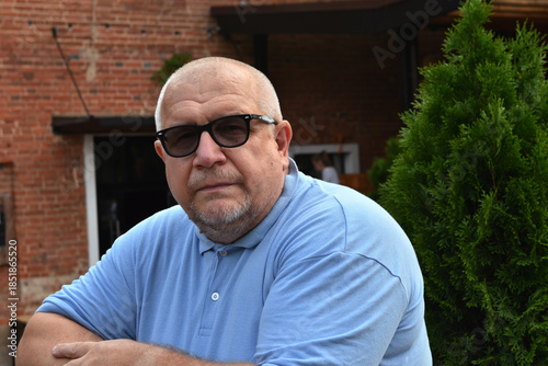 Portrait of a Caucasian elderly gray-haired man wearing glasses, against the background of a red brick wall of a house.