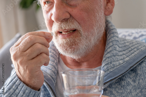 Senior man takes pill with glass of water in hand. Stressed elderly bearded man drinking sedated antidepressant meds. Man feels depressed, taking drugs. Medicines at work