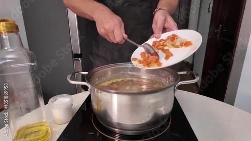 Men's hands add chopped vegetables, to boiling meat broth in a stainless steel pot on an induction cooktop