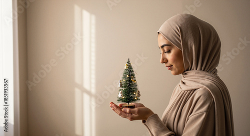 Muslim woman holding a small Christmas tree indoors with soft light  