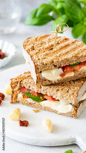 Delicious whole grain sandwich with fresh vegetables and creamy cheese on a marble cutting board
