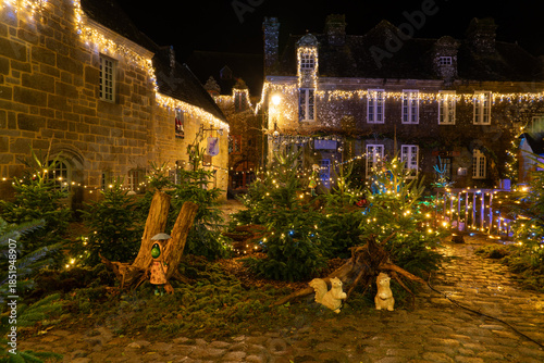 Place du village de Locronan en Bretagne décorée pour les fêtes de Noël, sapins et éléments lumineux installés devant les façades en pierre, ambiance nocturne festive et chaleureuse.