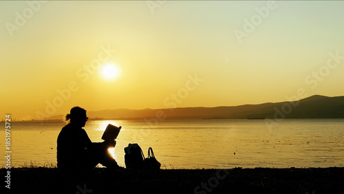 Woman Watching Sunset And Reading Book By The Sea
