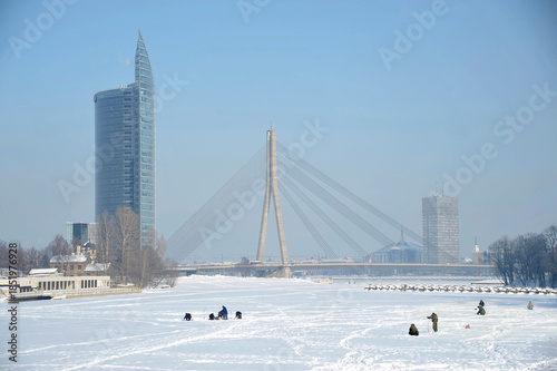 Ice fishing on the frozen Daugava River with Vanšu Bridge and skyline, Riga, Latvia