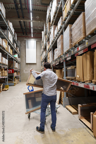 Man loading furniture panels onto shopping cart in warehouse aisle, home improvement, DIY shopping