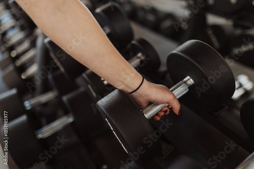 Quadro em tela Close-up shot of a fit young woman picking up a black dumbbell from a rack