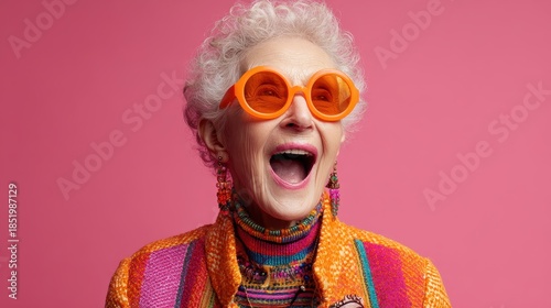 An elderly woman laughs joyfully while wearing a colorful jacket and oversized orange sunglasses, expressing confidence, fun, and vibrant personality.

