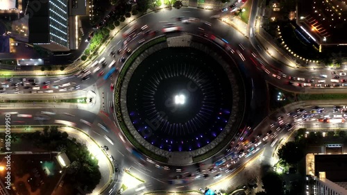 Aerial top-down hyperlapse of busy evening traffic flowing through the iconic Selamat Datang (Welcome) Monument roundabout in the central business district in Jakarta, Indonesia