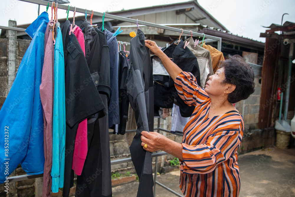 Obraz premium Elderly woman checking clothes on an outdoor drying rack, representing household chores, independence, and everyday senior lifestyle.