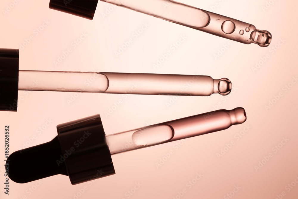 Fototapeta premium Three glass pipettes with facial serum on light orange background. Front view. Frontal close-up view of liquid gel or essential oil, banner for advertising anti-aging cosmetic product with bakuchiol,