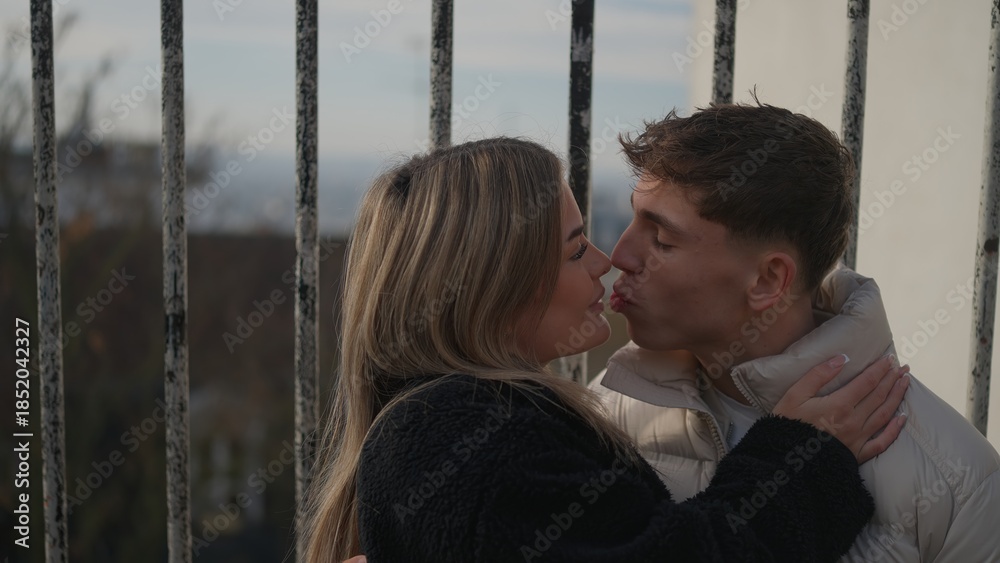 Obraz premium A young couple kisses affectionately in Paris France with a cityscape in the background. This image can be used to illustrate themes of love travel and romantic getaways.