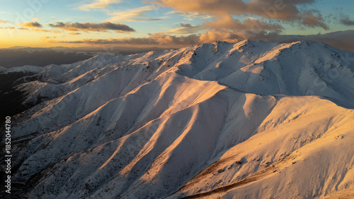 Snow covered mountain range bathed in warm sunlight during sunset or sunrise