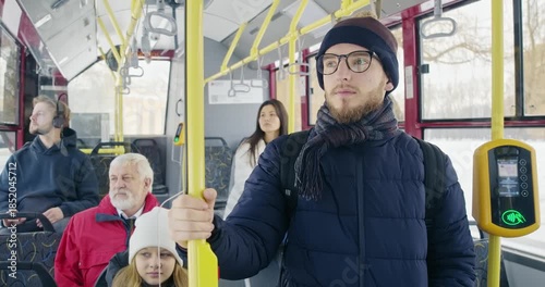 Front view of bus stopping at station, passengers waiting. Boy wearing sunglasses standing, pipe holding, girl, woman, old man, boy with earphones sitting. Concept of urban life.