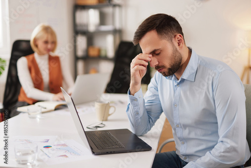 Cuadro en lienzo Man looks tired and stressed at his desk in the office while trying to solve business problems