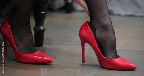 Close-up of a woman putting on red stiletto heels in a room
