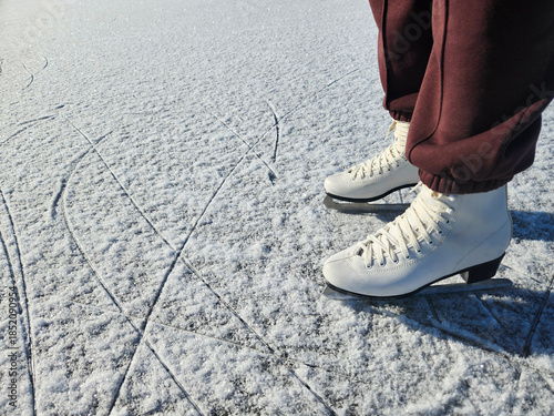 Female figure skater wearing white skates stands on smooth ice surface, showcasing balance and elegance in winter sports, with serene natural backdrop enhancing the scene