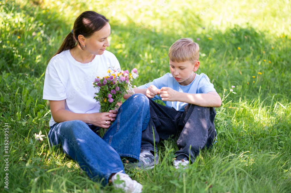 Fototapeta premium Teen boy giving mother bouquet of wildflowers on green lawn, family bonding outdoors