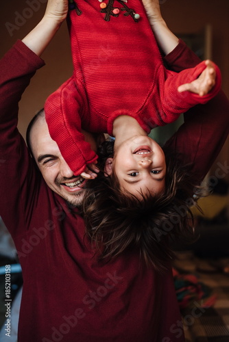 Happy father playing with his little daughter at home, lifting child upside down and laughing together