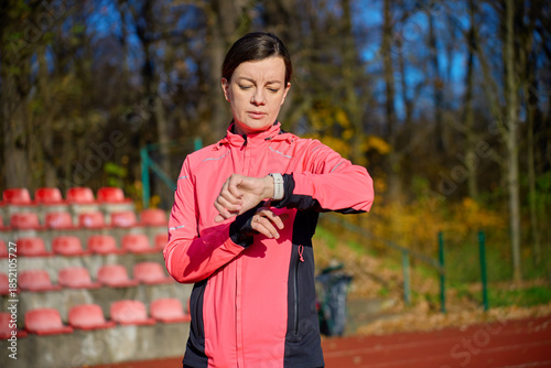 Woman wearing sports jacket checking smartwatch while standing on running track