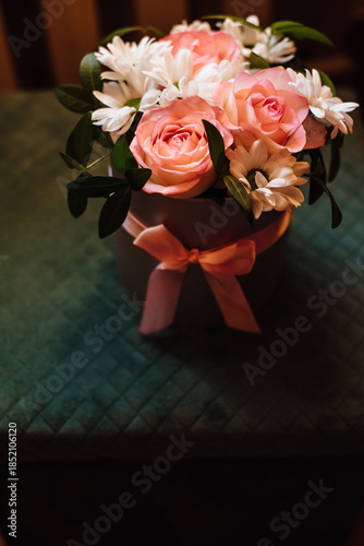 Elegant bouquet of pink roses and white daisies in a gift box with ribbon, soft light and cozy home atmosphere