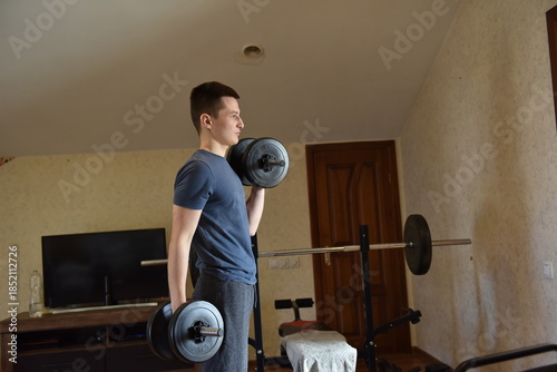 Young man lifting dumbbells during home workout in small apartment gym, strength training and fitness routine indoors