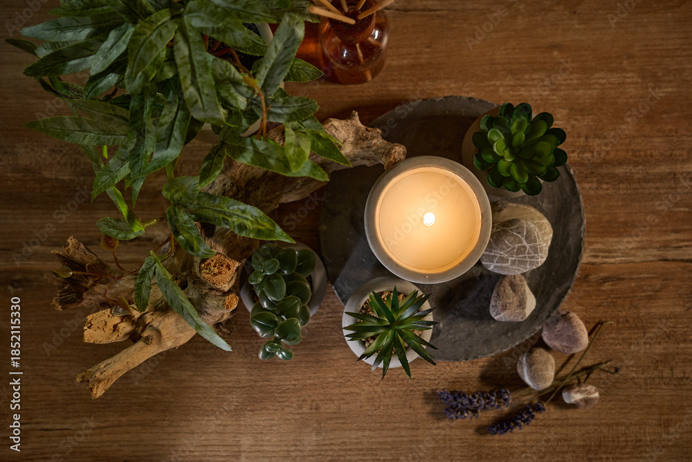 Fototapeta premium Candle on a stone surface surrounded by plants and decorative stones in a cozy indoor setting