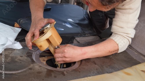 Automotive technician carefully installing a new fuel pump assembly into the gas tank of a modern vehicle during a repair service in a garage, showcasing a complex maintenance procedure