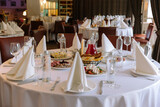 Round banquet tables set with white tablecloths, snacks, appetizers, and drinks in a restaurant for a wedding or event