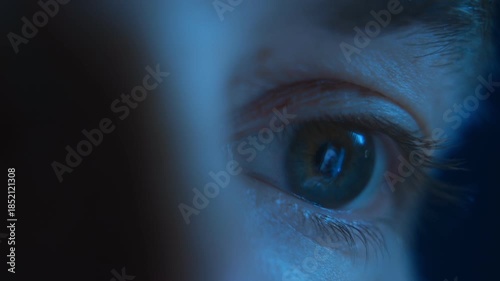 Macro shot of a tired human eye looking at glowing smartphone screen and reflects social media feed, illuminated with blue light at night. Eyestrain, digital addiction or insomnia concept