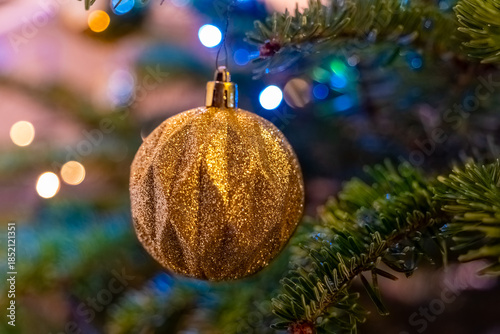 Golden ornament hangs gracefully on a festive Christmas tree adorned with shimmering lights