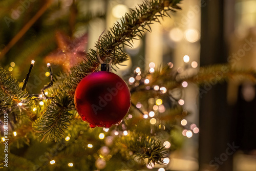 Shining red ornament hanging from green pine branch surrounded by festive lights in a winter wonderland