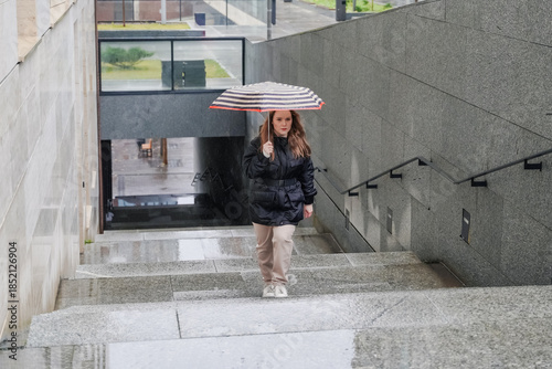 Approaching staircase with umbrella in rainy city. Stopping on wet steps near underpass entrance. Commuting pedestrian travel, bad weather, rain protection, waterproof canopy, urban street. Transit.