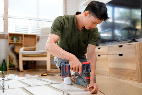 Man assembling purchased furniture in beautiful room with large window. Concept of DIY or furniture assembly services