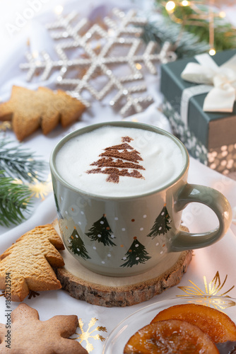  A cup of hot coffee latte with latte art draw Christmas tree on its foam, with festive ambiance and decorative with candied orange and cookies. 