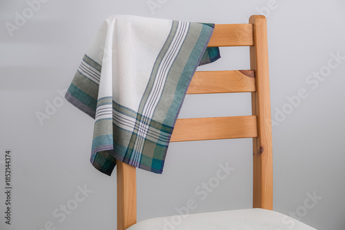 A folded white handkerchief with green and grey stripes is draped over the wooden backrest of a chair.