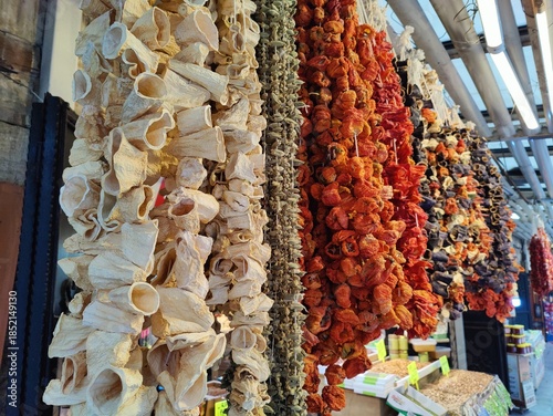 Rows of traditional sun-dried eggplants and red peppers hanging on strings in a Turkish spice market, essential ingredients for making stuffed vegetable dishes.