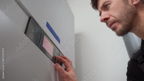 Man adjusting control panel on heat pump inside modern home during installation. Concept of home heating, energy efficiency and HVAC maintenance