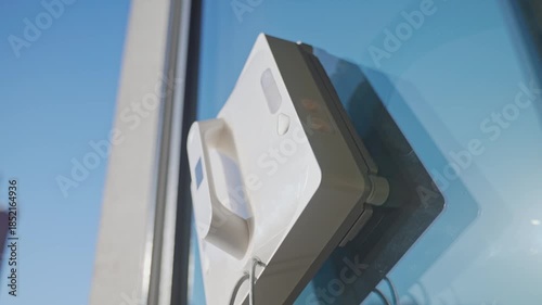 Square window cleaning robot washing glass. Robotic window cleaner working on window surface against blue sky. Smart home appliance concept