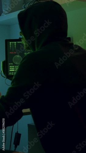 Hooded figure engaged in intense computer work at a desk with multiple screens displaying data, camera follows action with smooth dolly movement towards the subject