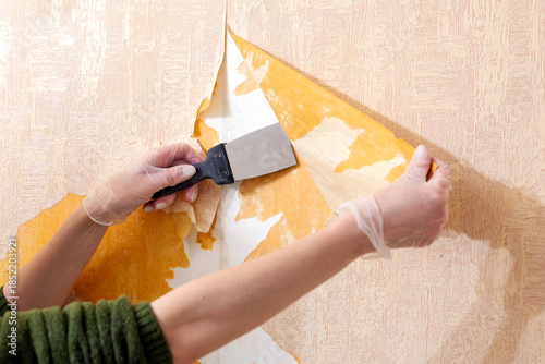 A woman is tearing old wallpaper off the wall.