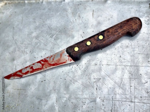 Kitchen knife with wooden handle and blood stains on the blade lying on a scratched metal surface