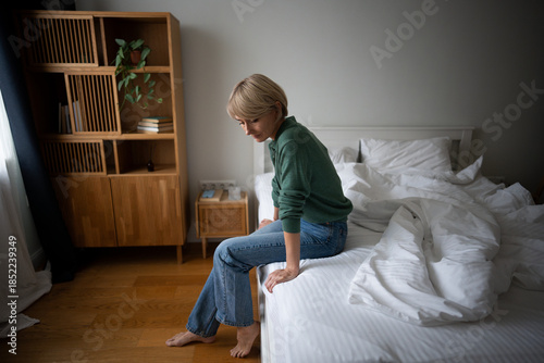 Foto Depressed upset middle aged woman fully dressed sitting on bed in morning looking at side and thinking deeply, dealing with loneliness after divorce, coping with burn out and autumn blues weakness