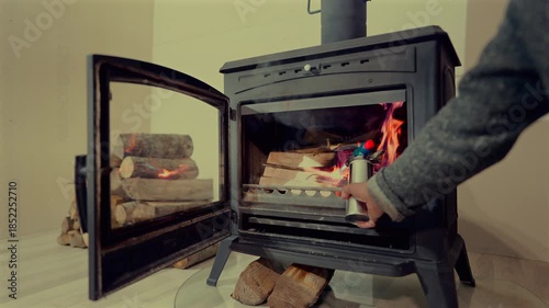 Burning wood stove. Person use gas burner  to light fire in wood stove. Wood logs stacked at iron stove. Cast iron stove with burning wood inside. Winter, atmosphere feels inviting.